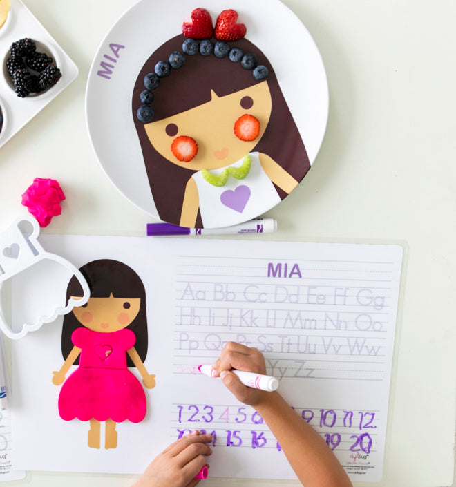 Dylbug personalized placemat in purple. Placemat is double sided including an activity side with letter tracing and customized face side. Little girl writing on activity side.