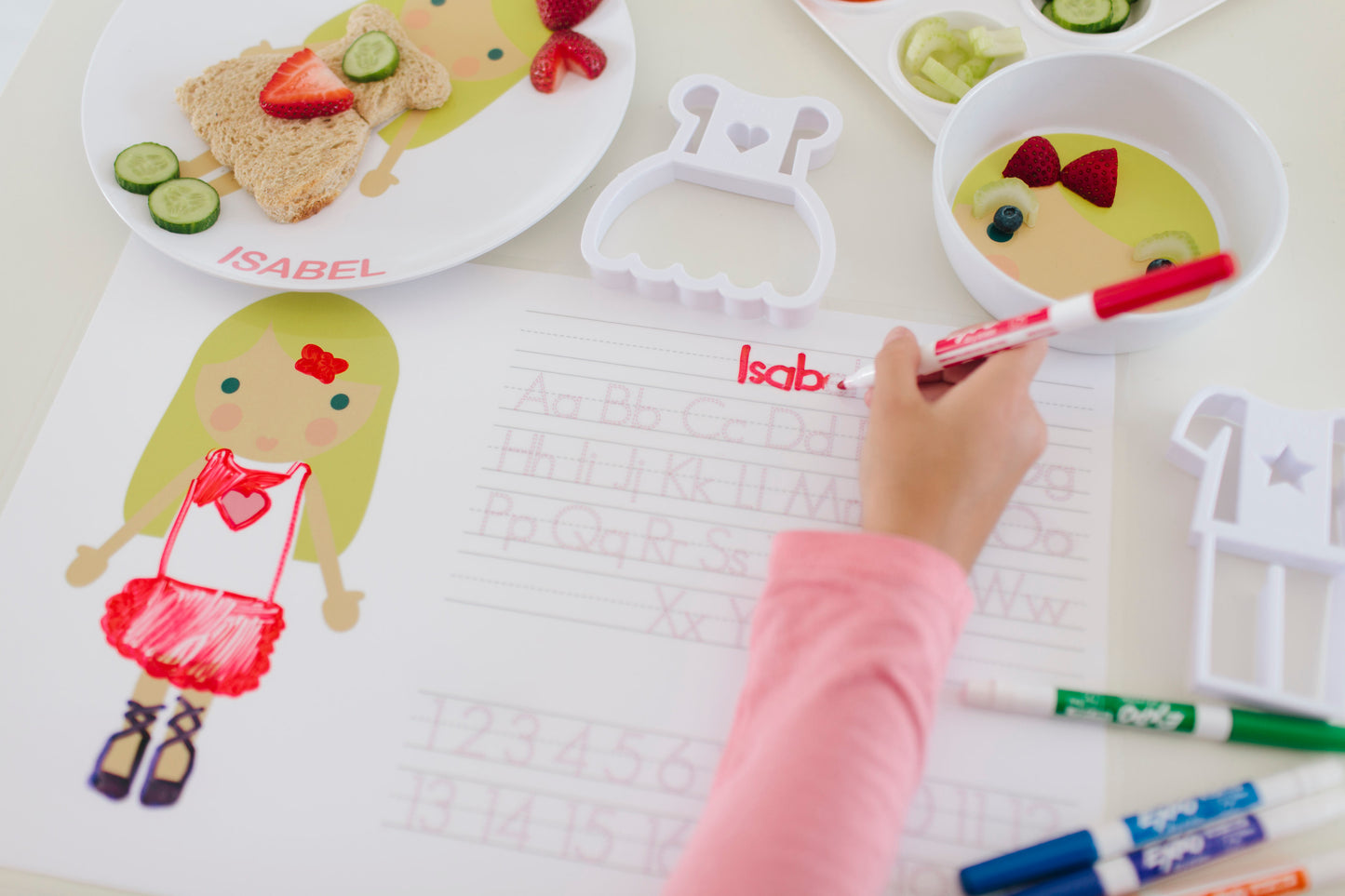 Dylbug personalized placemat in pink. Placemat is double sided including an activity side with letter tracing and customized face side. Little girl using activity side and spelling her name.