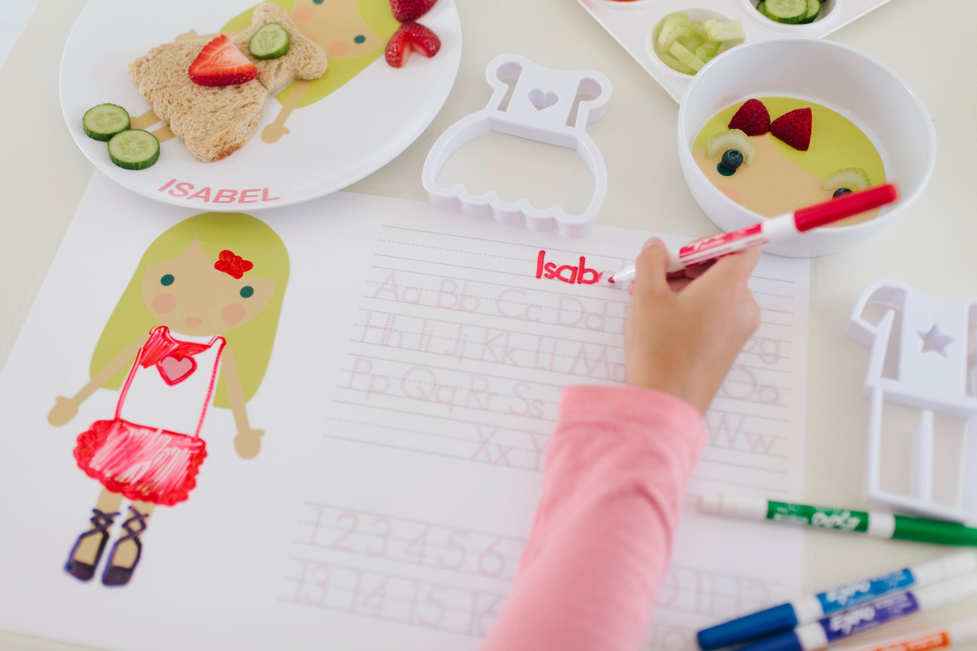 Dylbug personalized placemat in pink. Placemat is double sided including an activity side with letter tracing and customized face side. Little girl using activity side and spelling her name.