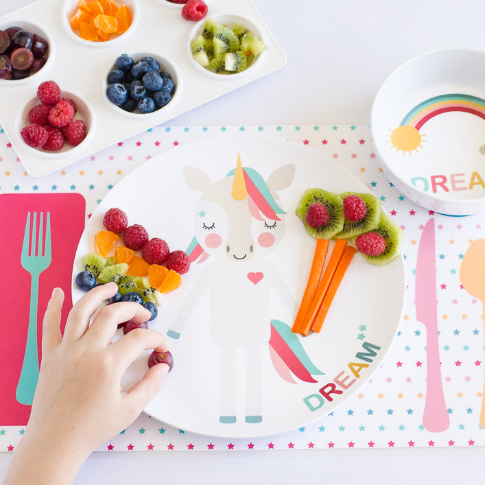 Dylbug Imagination Plate and Dishes Collection showcasing the pink unicorn dream plate with pink unicorn placemat and dream unicorn bowl. using fruits and veggies to create and decorate her plate